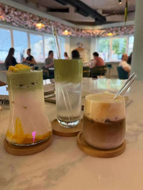 Drei Matcha- und Kaffeegetränke auf einem Marmortisch, im Hintergrund der Gastraum